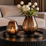 Tasman ribbed windlicht en vaas van VTW op een dienblad op een ronde salontafel, met een brandende kaars en witte bolbloemen