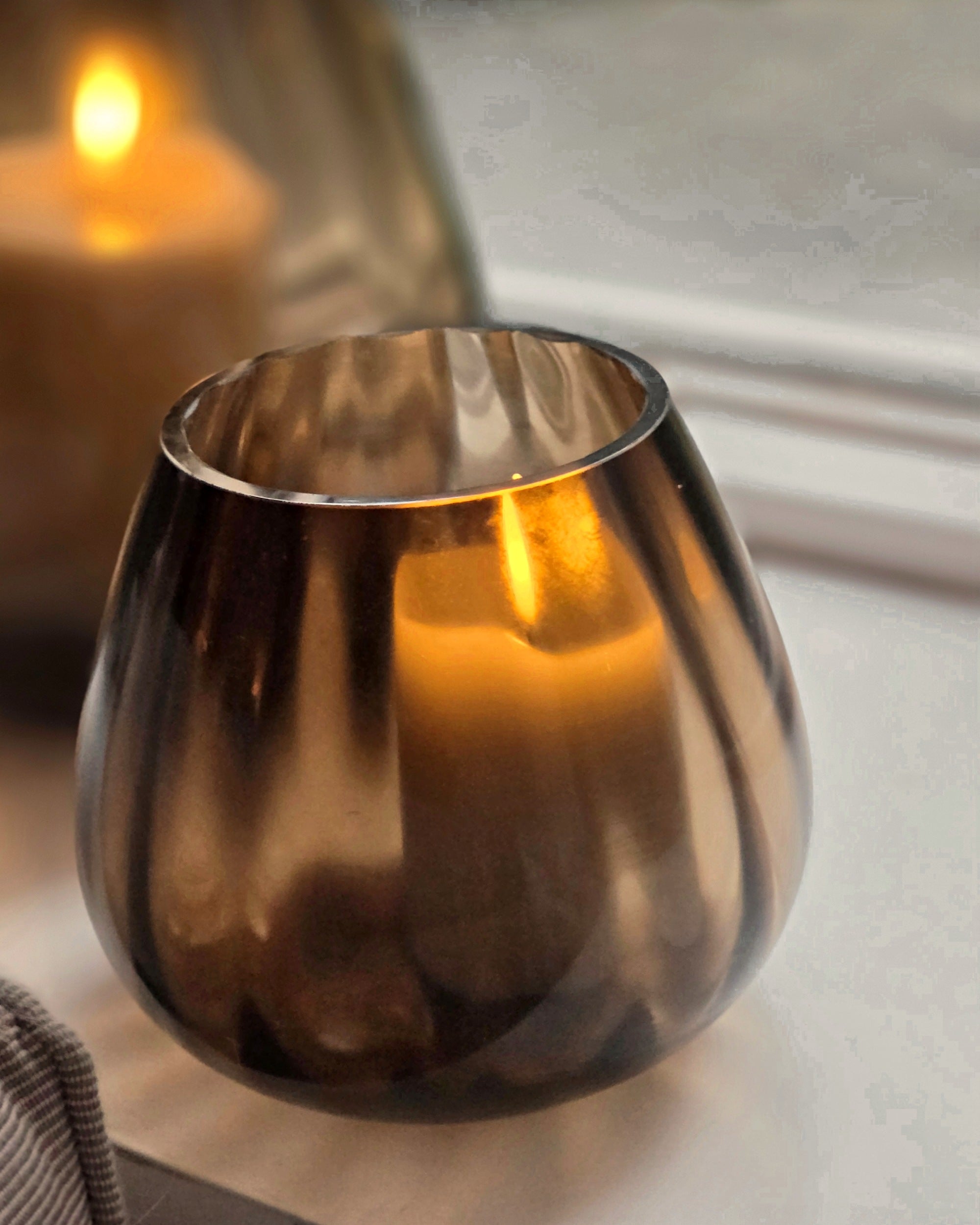 Kleine Tasman ribbed dark taupe met kaars, het licht schijnt gestreept door het glas